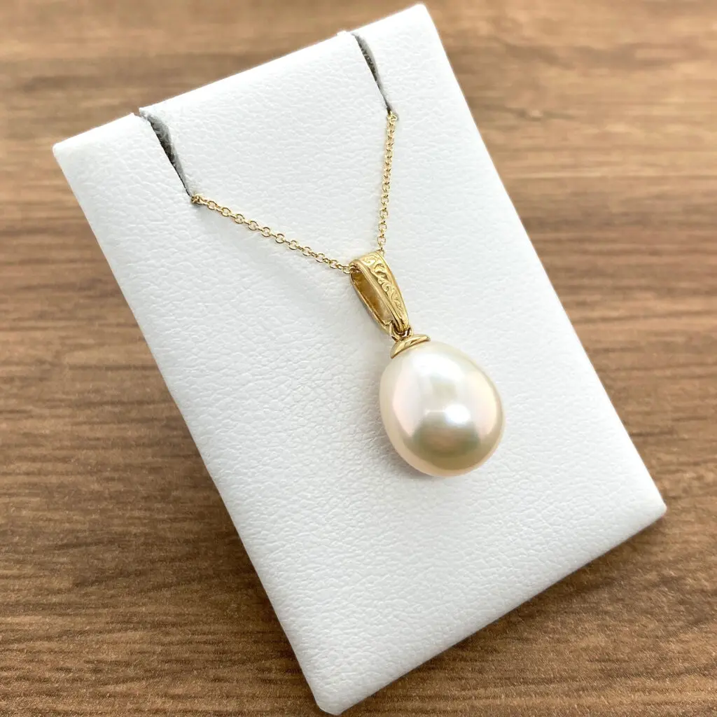 A white pearl pendant on a yellow gold chain on a wooden table.