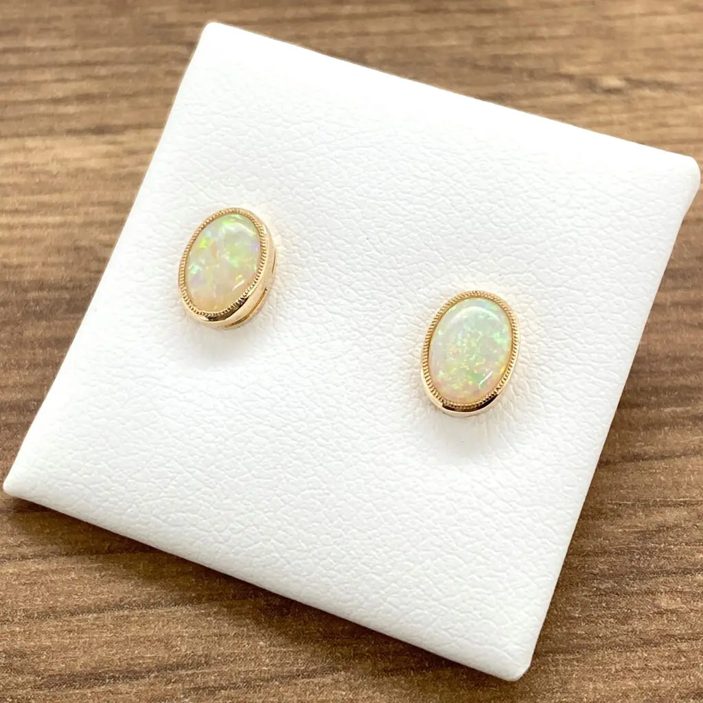 Gold opal stud earrings on white background.