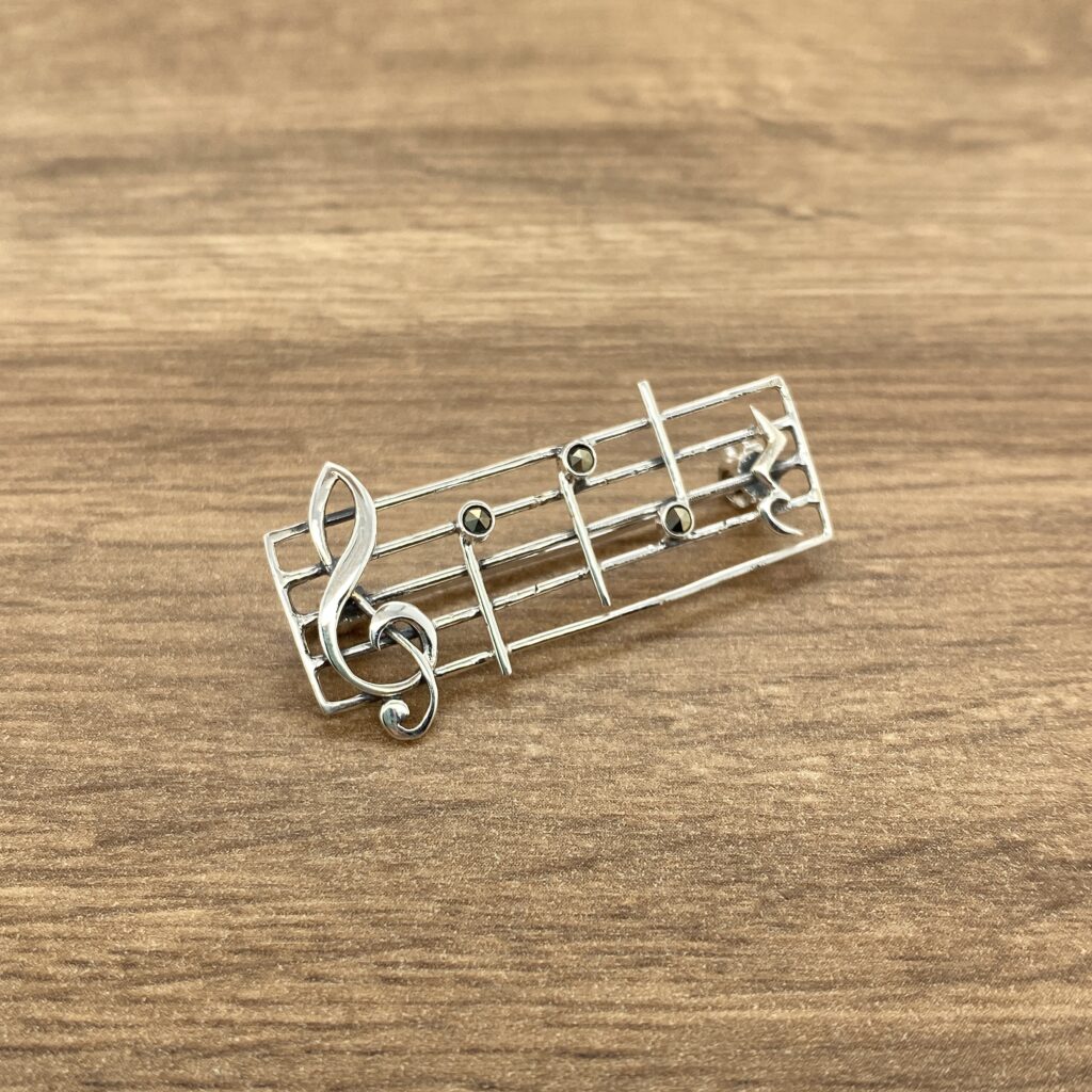 A silver music note brooch on a wooden table.