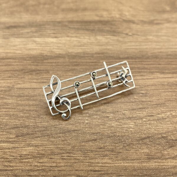 A silver music note brooch on a wooden table.