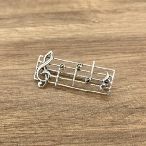 A silver music note brooch on a wooden table.