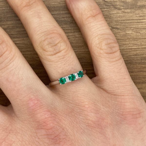 Emerald and diamond ring on finger.