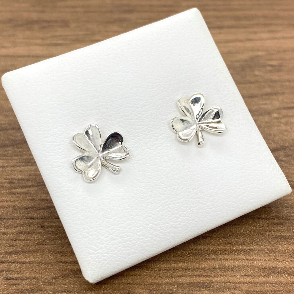 Silver shamrock stud earrings on white background.