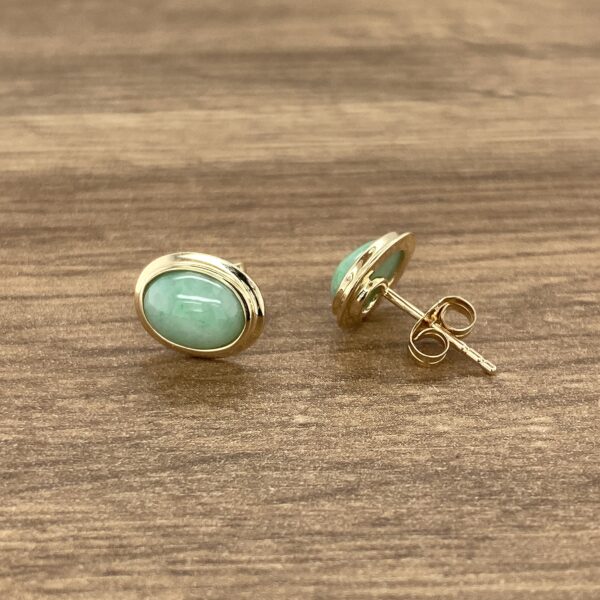 Gold oval jade earrings on wood.