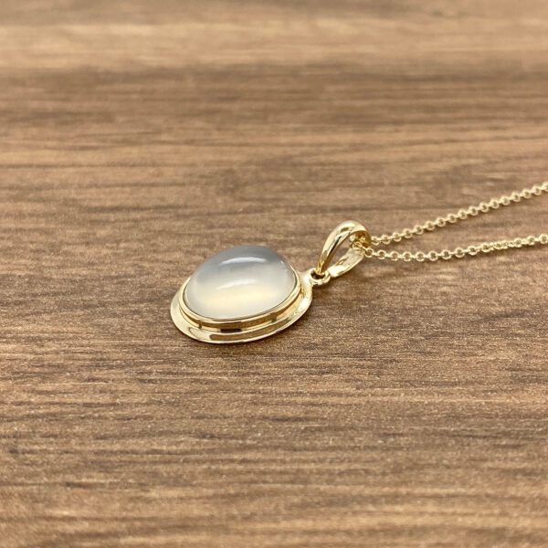 Gold necklace with a white oval gemstone.