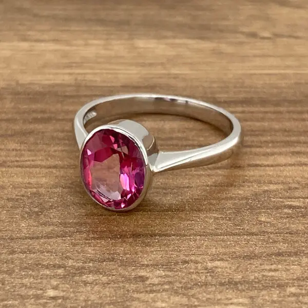 Pink gemstone ring on wooden surface.