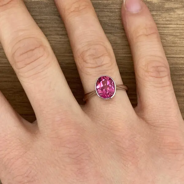 Pink oval gemstone ring on finger.