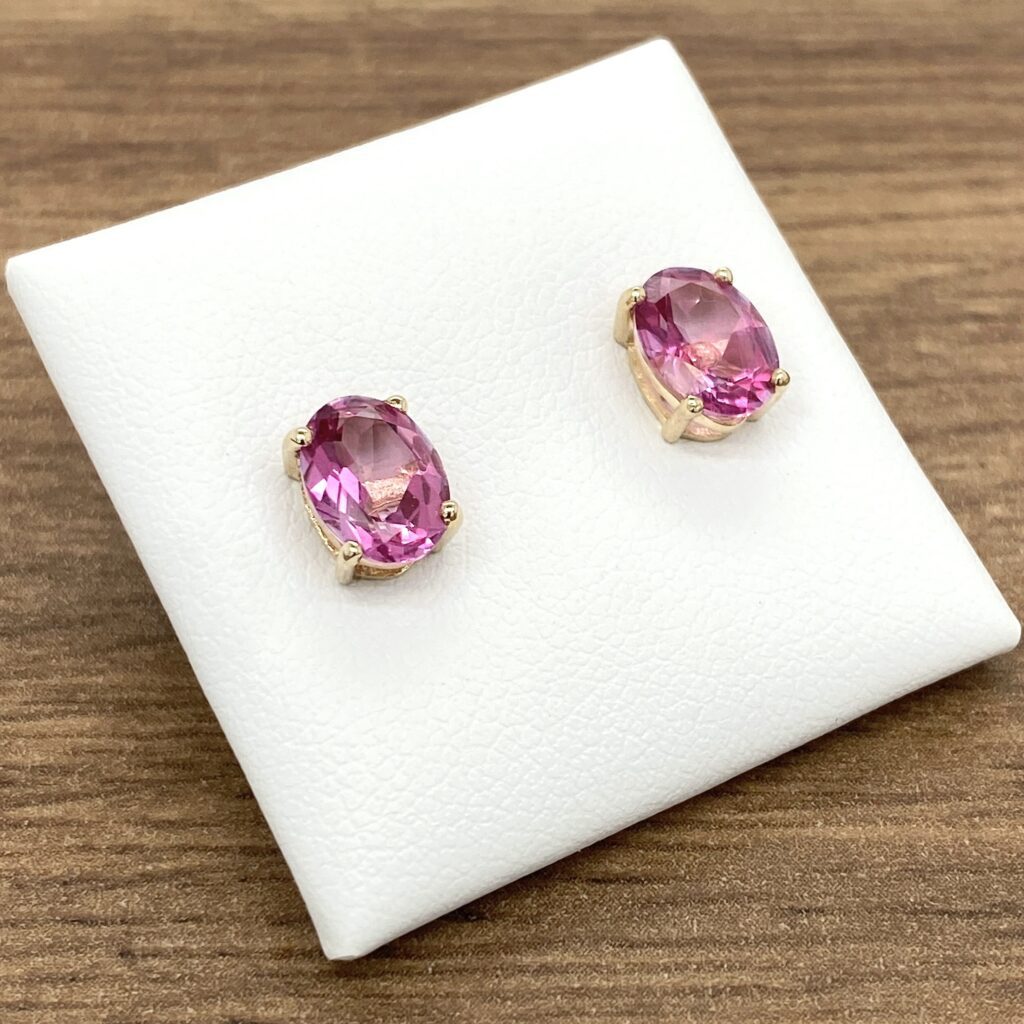 Pink oval gemstone earrings on white background.