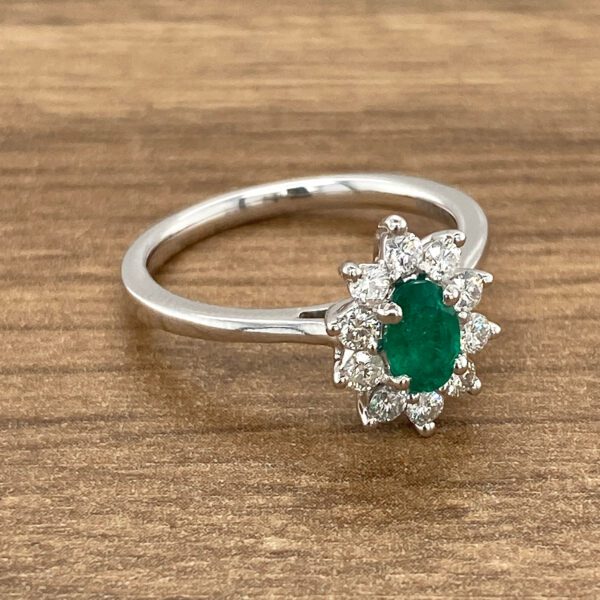 Emerald and diamond halo ring on wood.