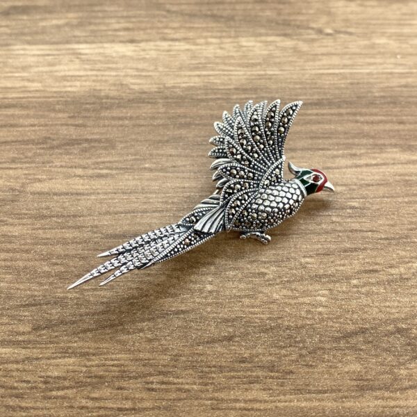 Silver pheasant brooch with red eye.