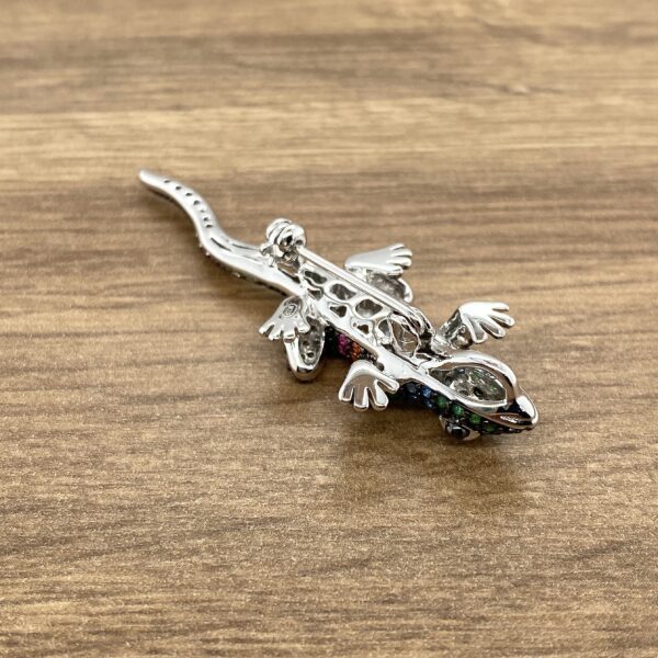 Gemstone lizard brooch on a wooden surface.