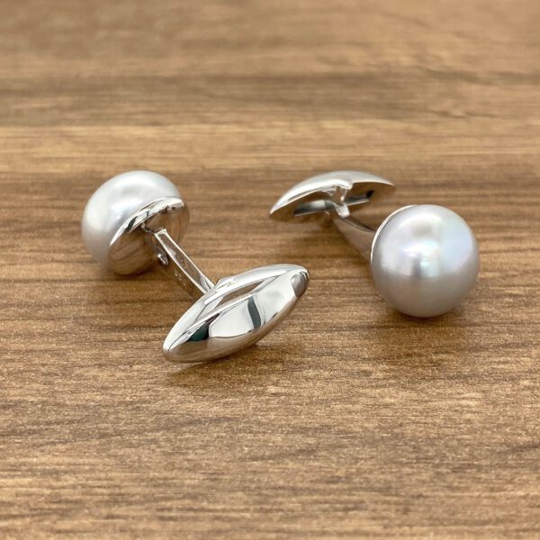 Silver pearl cufflinks on wood.