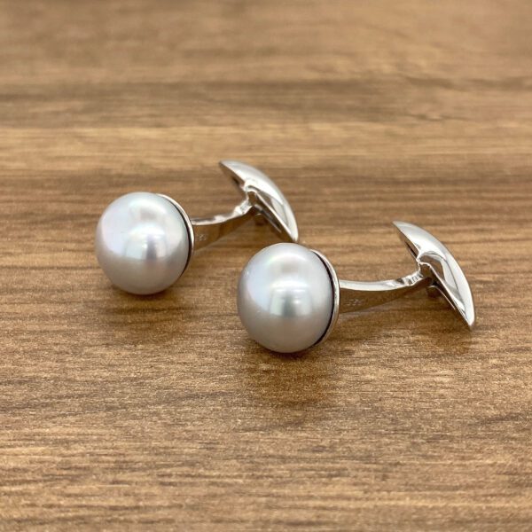 Silver pearl cufflinks on wood.
