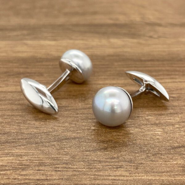 Silver pearl cufflinks on wood.