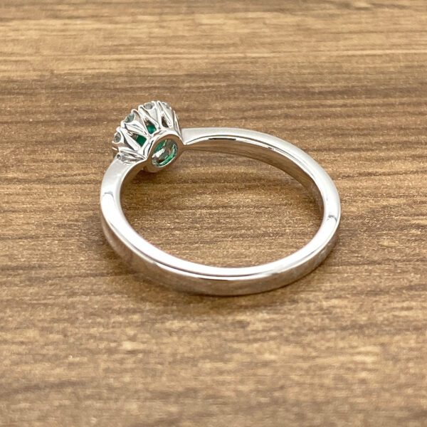 Emerald and diamond ring on wood.