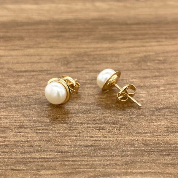 Gold pearl stud earrings on wood.