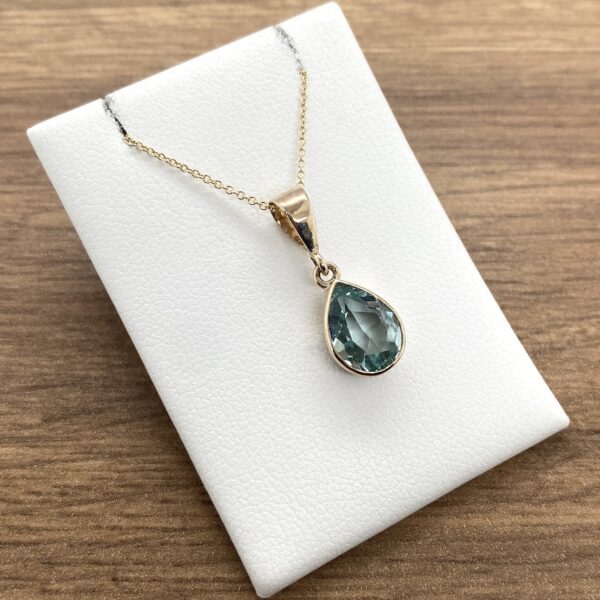 Gold necklace with pear-shaped blue gemstone.