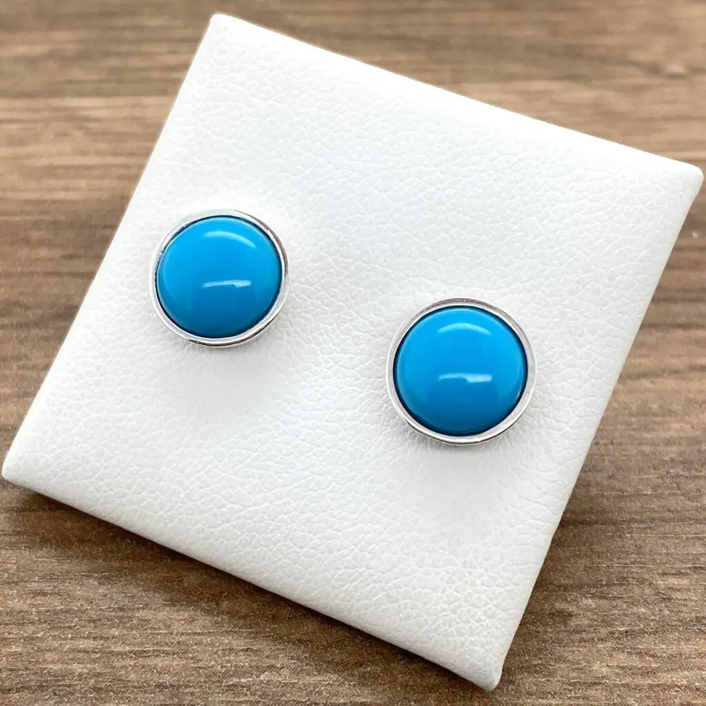 Turquoise stud earrings on white display cushion.